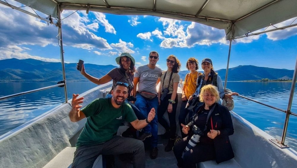 Tourists smiling and enjoying a scenic boat trip on Lake Kerkini to see pelicans.